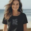 A woman on a beach is wearing a black t-shirt with the message "ME WE we are one" printed on it.
