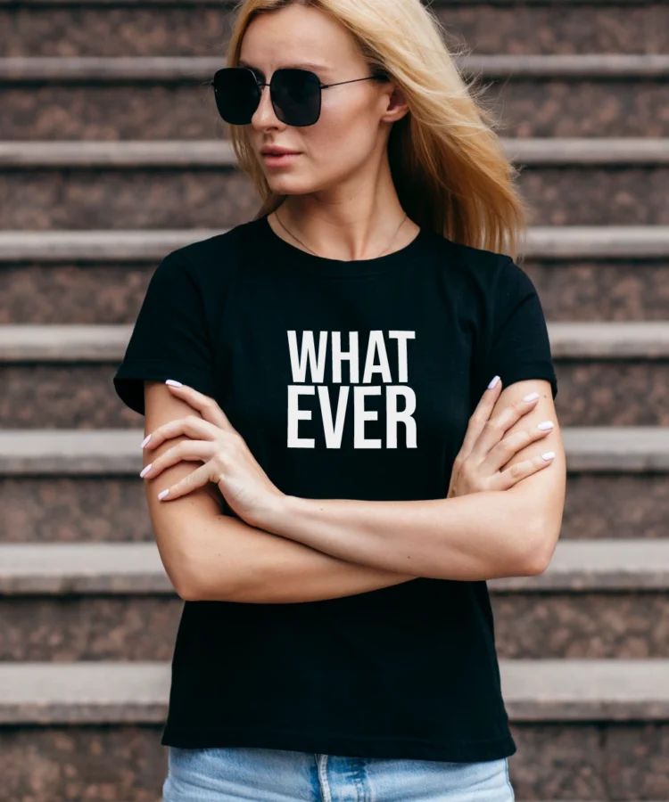 Naine mustas “WHAT EVER” T-särgis, päikeseprillid, käed ristis trepiastmetel; lifestyle-foto.