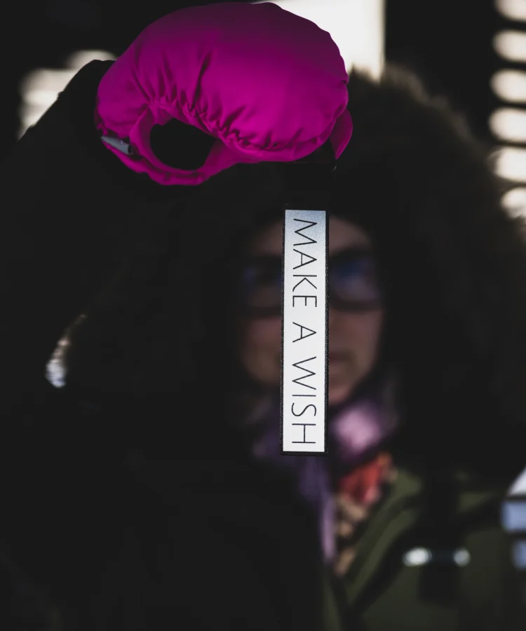 Inimene roosas talvekinnas hoiab püstises asendis helkur võtmehoidjat tekstiga “MAKE A WISH”, taust hägus, talveriided.