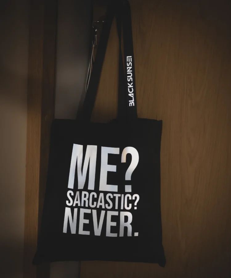 Blacksunset must tote “ME? SARCASTIC? NEVER.” – valge front-print, külgsildiga kott; lifestyle-kaader.