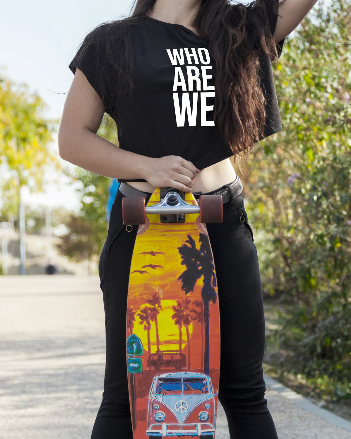 Must T-särk tekstiga “WHO ARE WE”, inimene hoiab püstist longboardi – urban lifestyle-kaader; Blacksunset brändi visuaal.