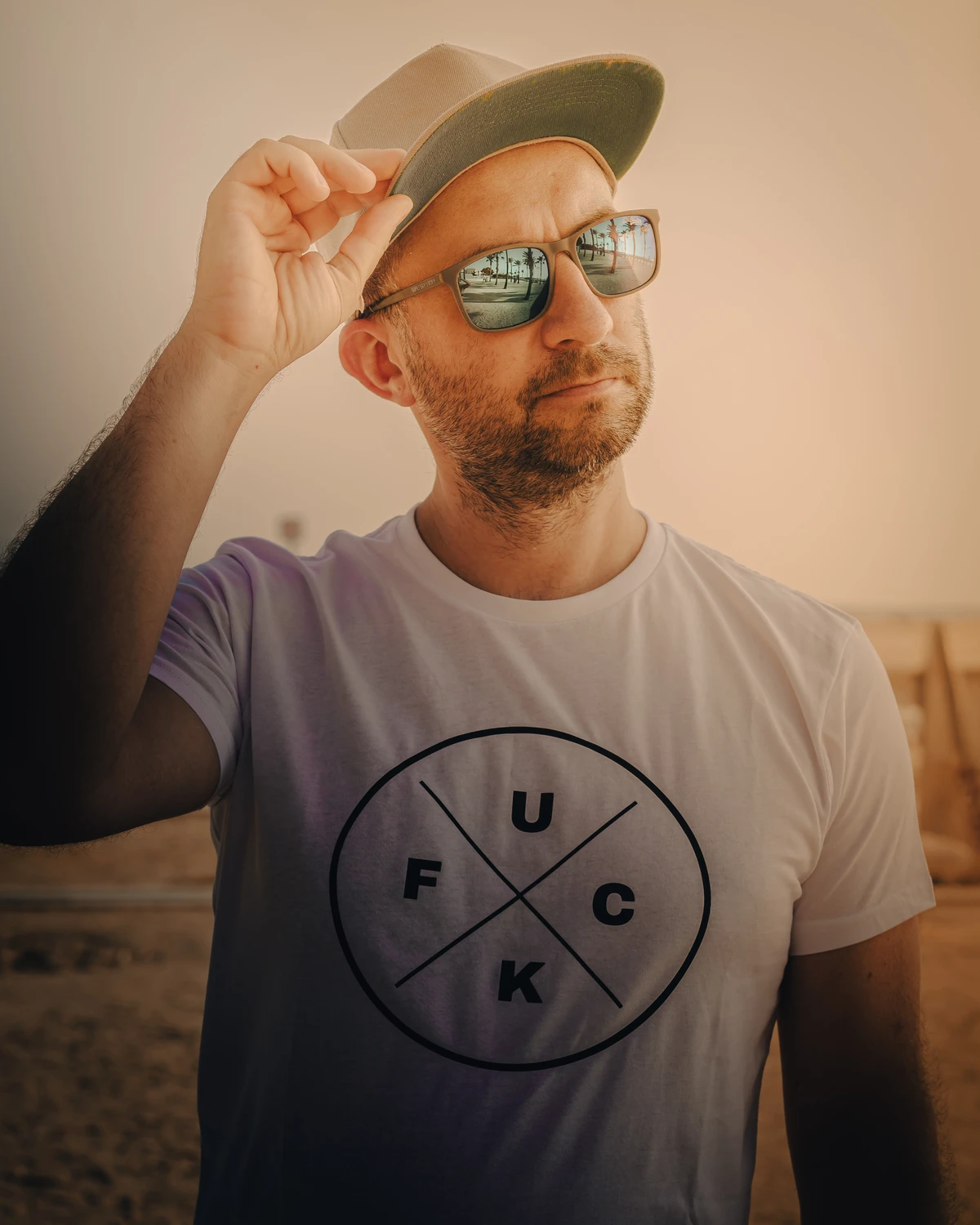 Minimalist portrait of a man in sunglasses and a hat; round graphic on T-shirt, warm light and shallow depth of field. Anti Soosaar.