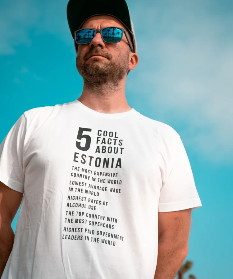 Mees kannab valget Blacksunset “5 Cool Facts About Estonia” T-särki; päikeseprillid ja nokkmüts, sinine taevas taustal.