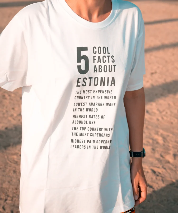Valge Blacksunset “5 Cool Facts About Estonia” T-särk modellil rannaliival; vertikaalne tekstidisain.