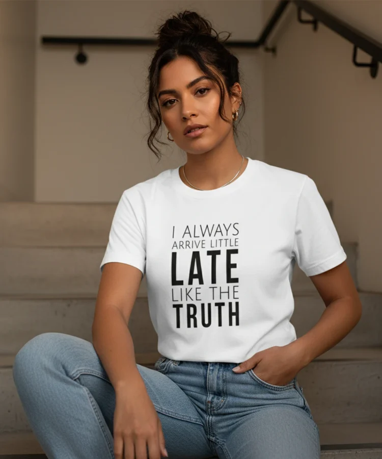 Blacksunset unisex valge T-särk „I ALWAYS ARRIVE LITTLE LATE LIKE THE TRUTH”; naismudel istub betoonastmetel, casual stiil, õhtuvalgus.
