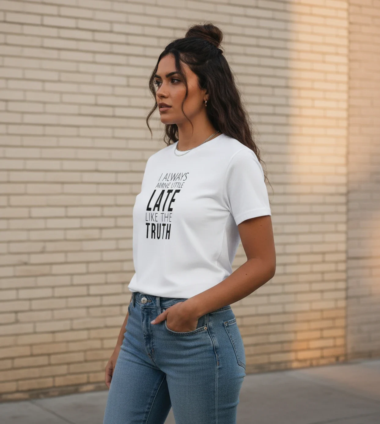 Blacksunset unisex valge T-särk „I ALWAYS ARRIVE LITTLE LATE LIKE THE TRUTH”; ¾ vaade, käsi taskus, hele tellissein ja linnatänav taustal.