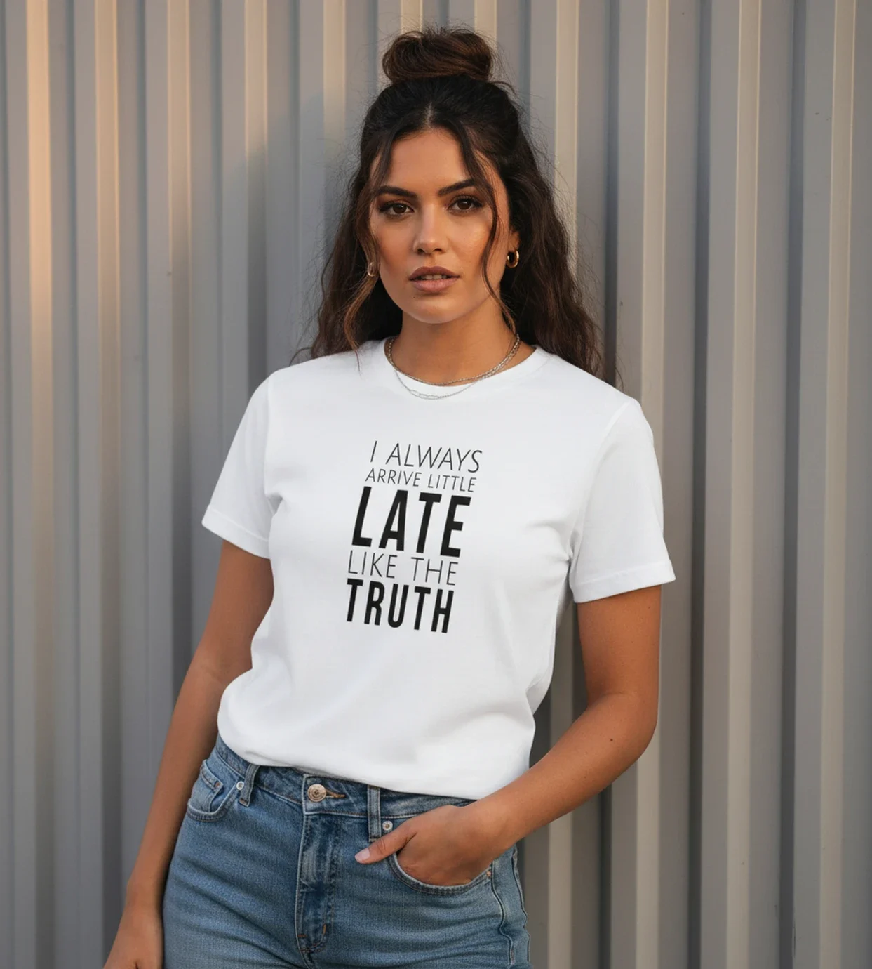 Blacksunset unisex valge T-särk „I ALWAYS ARRIVE LITTLE LATE LIKE THE TRUTH”; sirge eesvaade, hall vertikaalne metallsein taustal, minimalistlik look.