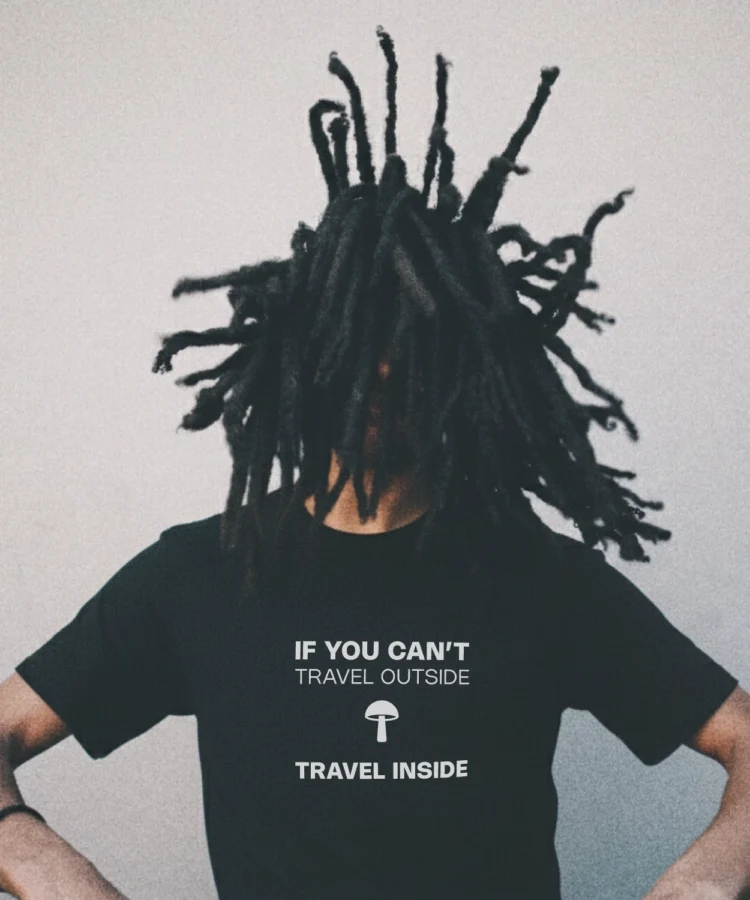 Blacksunset must unisex T-särk „IF YOU CAN’T TRAVEL OUTSIDE / TRAVEL INSIDE”; valge kiri ja seen, modell liikumises, graanuline urban taust.