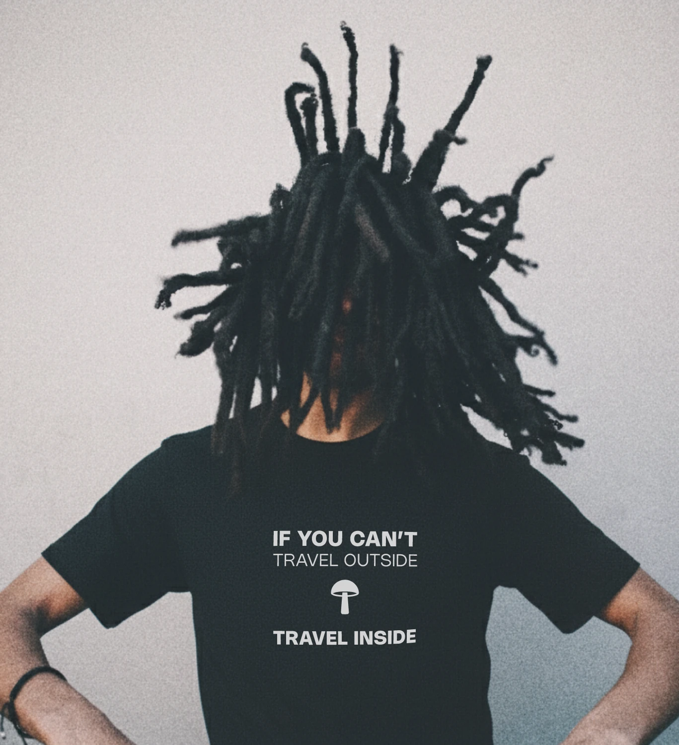 Blacksunset must unisex T-särk „IF YOU CAN’T TRAVEL OUTSIDE / TRAVEL INSIDE”; valge kiri ja seen, modell liikumises, graanuline urban taust.