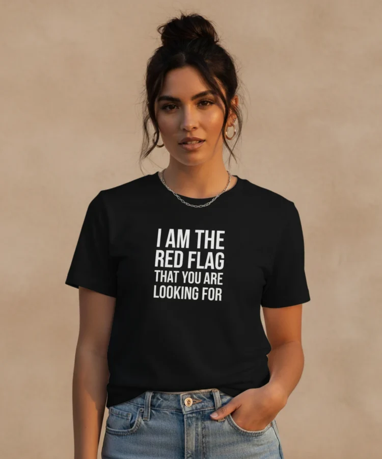Blacksunset unisex must T-särk “I AM THE RED FLAG THAT YOU ARE LOOKING FOR”; naismudel ¾ eesvaade, valge kiri, soe õhtuvalgus, neutraalne sein.