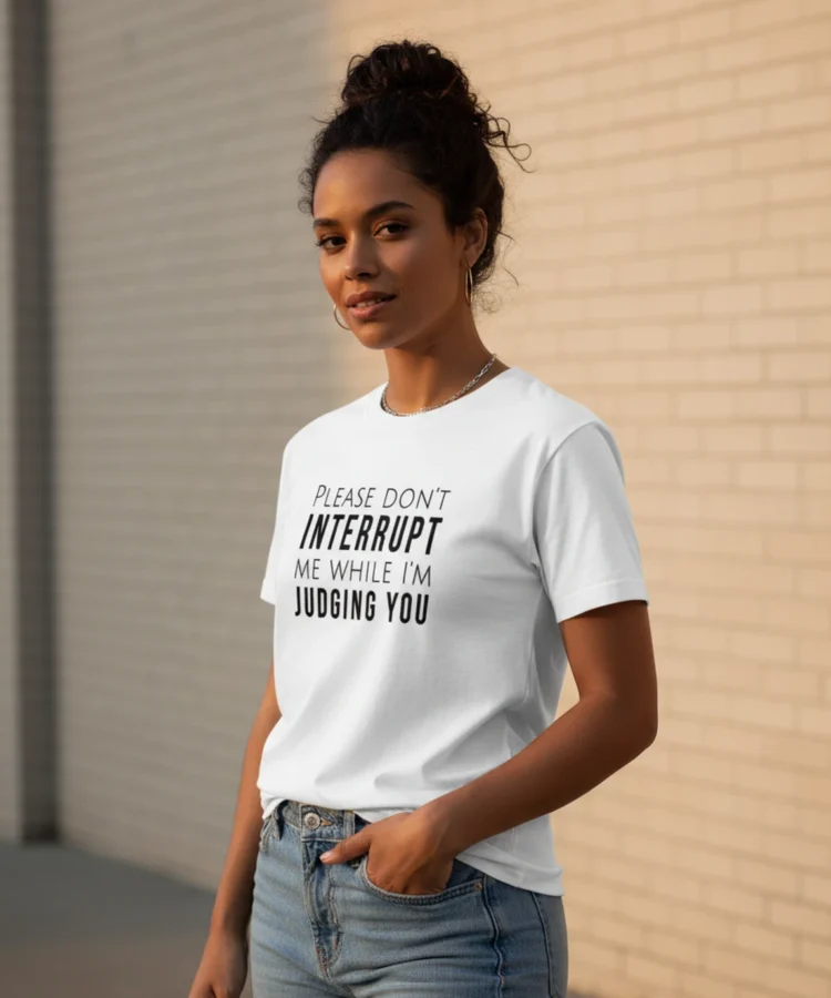 Blacksunset unisex valge T-särk PLEASE DON'T INTERRUPT ME WHILE I'M JUDGING YOU — must tüpograafia; naismudel 3/4 eesvaade, hele tellissein.