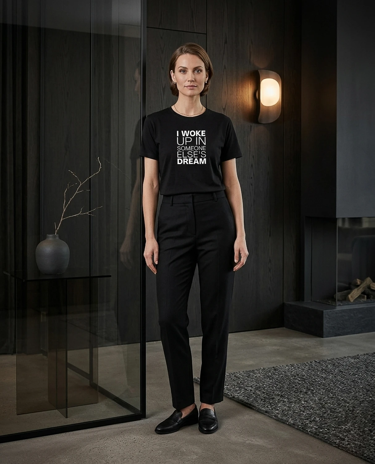 A woman wears a black I Woke Up In Someone Else's Dream T-shirt in a dark interior