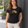 Carolina wears a black fitted women’s T-shirt with a gold sleepy hedgehog design beside a dark timber wall.