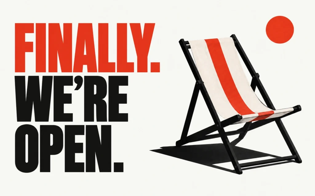 A light poster reading “FINALLY. WE’RE OPEN.” beside an open deckchair with a black frame and red-striped canvas.