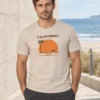 Rasmus kannab liivakarva California unisex T-särki rannapromenaadil heleda kiviseina kõrval.