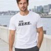 Rasmus kannab valget unisex T-särki musta Nothing to read here kirjaga veeäärsel promenaadil.