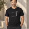 Rasmus wears the black unisex Raamist väljas T-shirt beside a pale courtyard wall. The white square frame is centred on the shirt with a dot above and to its right.